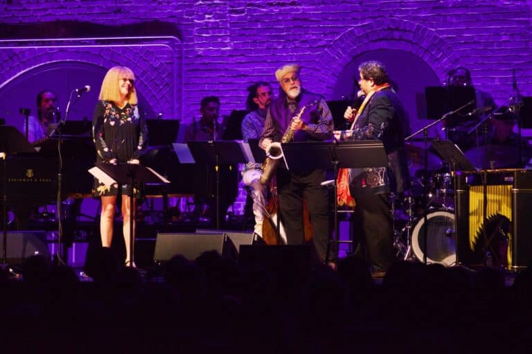 Karen Mantler, Joe Lovano and Arturo O'Farrill stand on stage in front of the Afro Latin Jazz Orchestra.