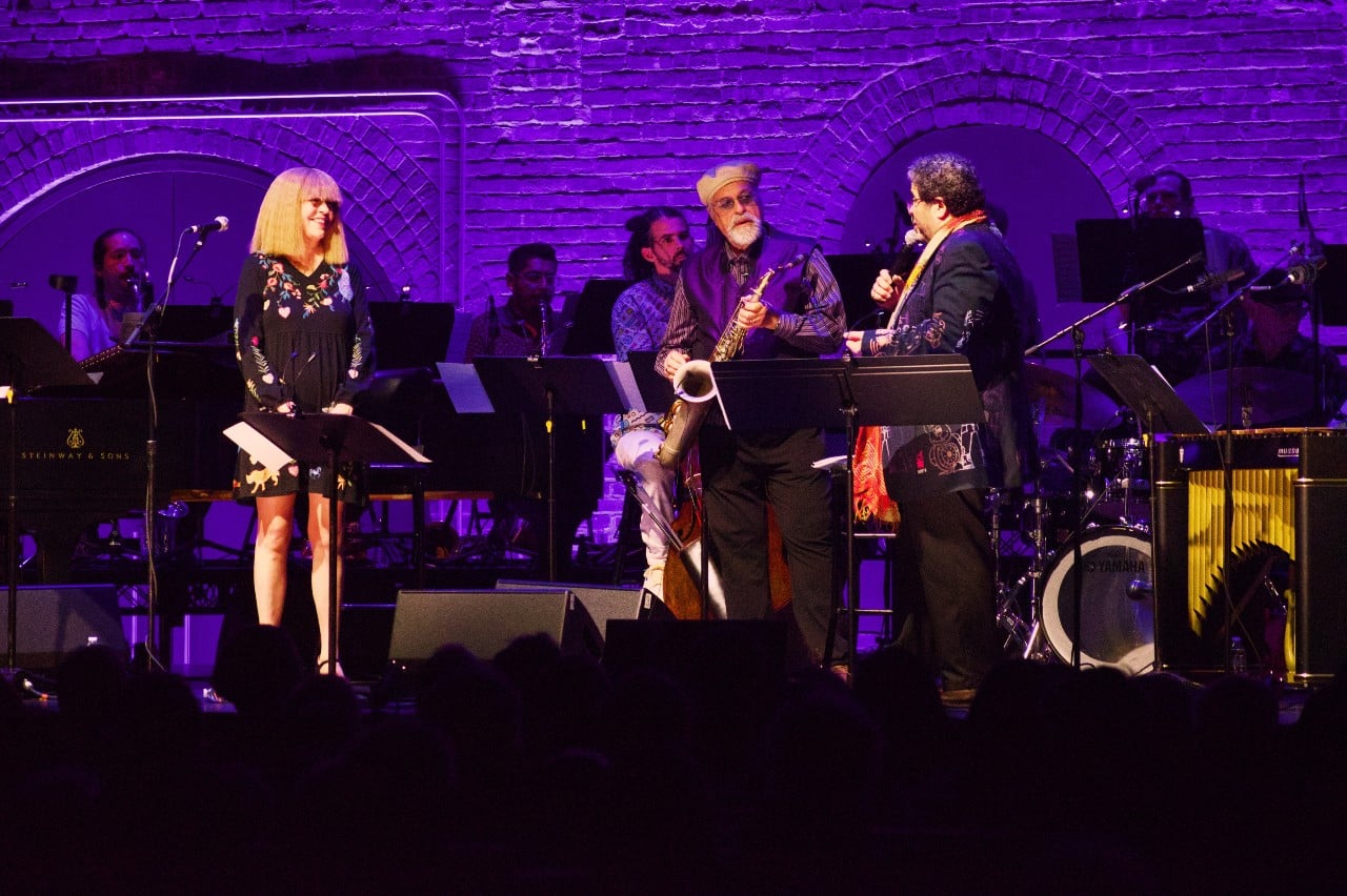 Karen Mantler, Joe Lovano and Arturo O'Farrill stand on stage in front of the Afro Latin Jazz Orchestra.