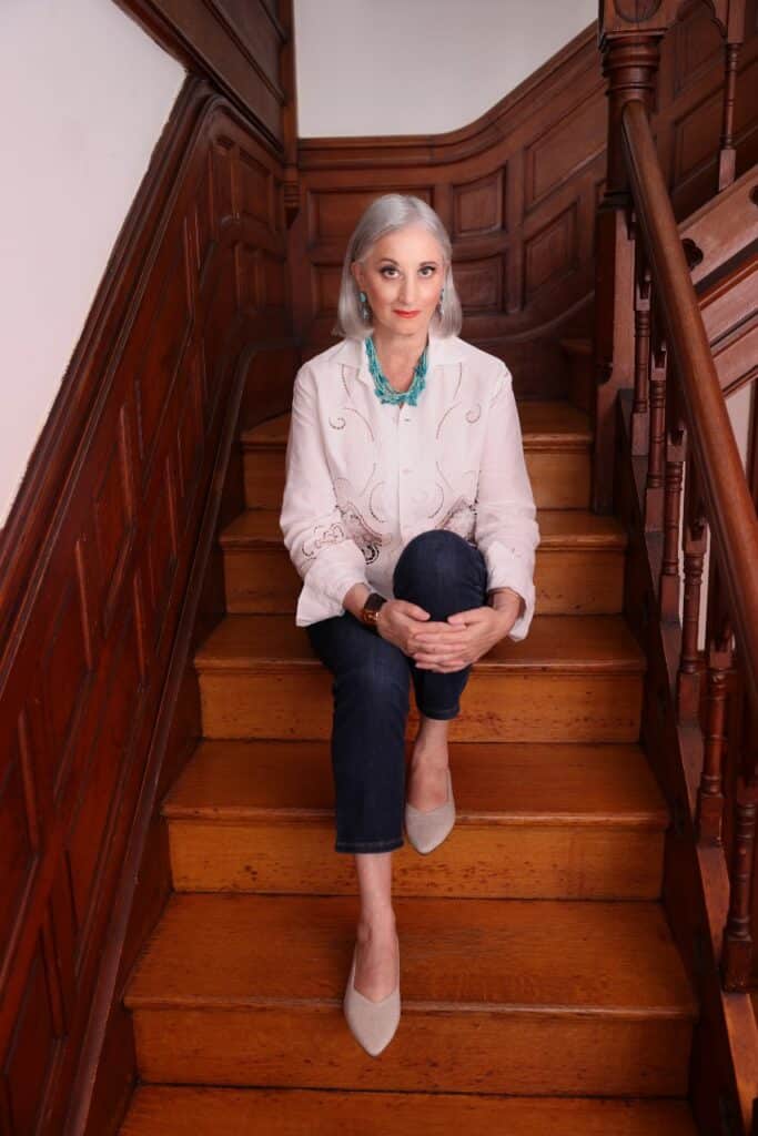 Renee Rosnes sits on some ornate wooden stairs, looking directly into camera.