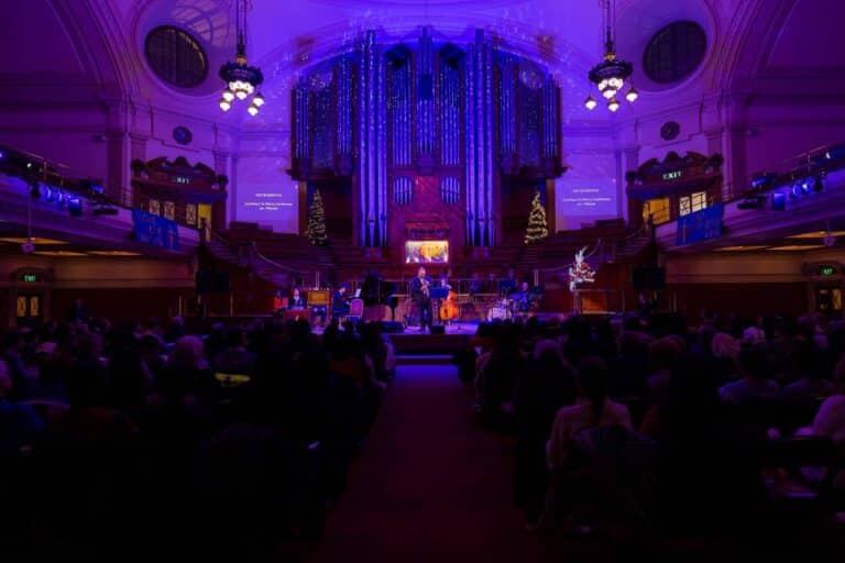 Musicians on a festive stage in a large, ornate building.