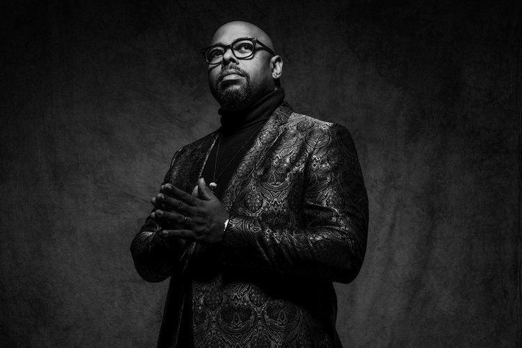 Christian McBride black and white image, wearing suit and glasses looking upwards