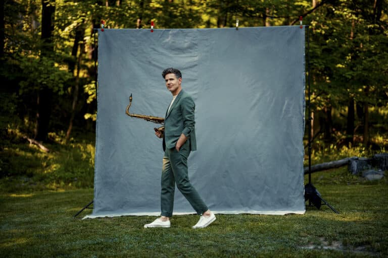 Ben Wendel stands in the middle of the frame, mid walk, saxophone tucked under his arm.