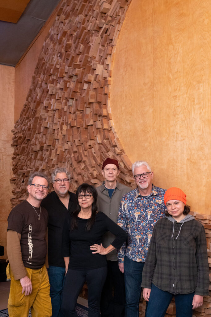 Musicians for Schoenberg on the Beach album lined up together with an art installation in background