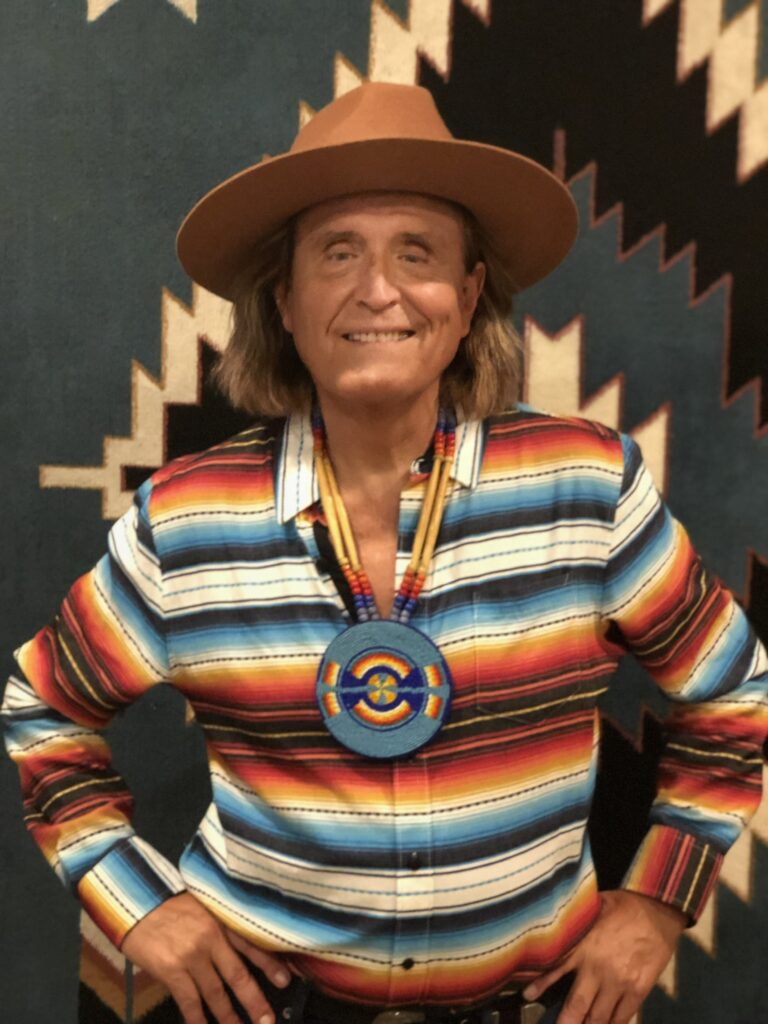 Garrett Saracho wearing a stripey colourful shirt, hat and smiling at the camera