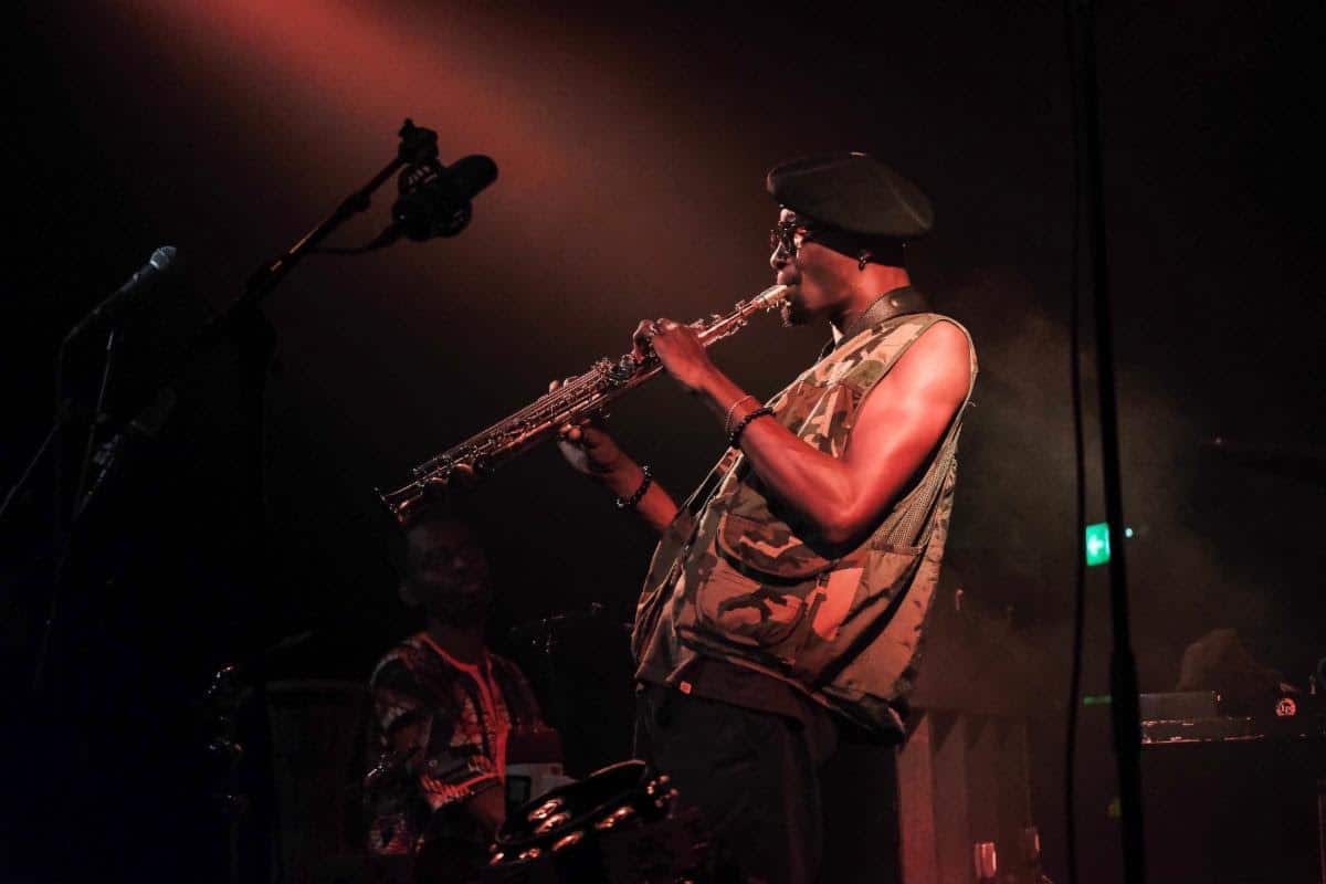 Isaiah Collier plays saxophone on stage under dramatic red lighting.