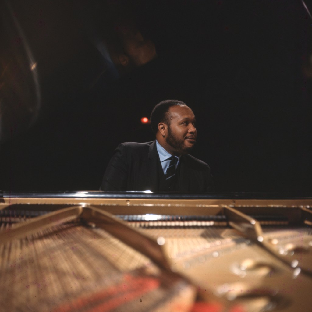 Shot of Les McCann from over the piano, as he plays and looks mischievously to the side.