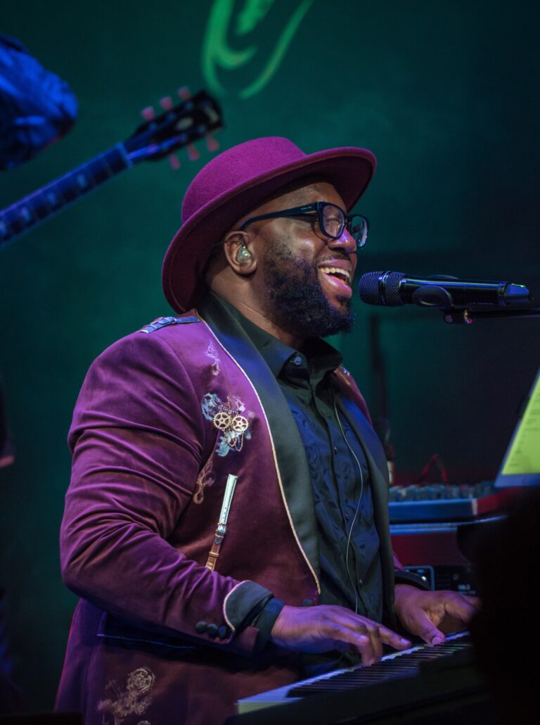 Luke Smith wearing a purple velvet suit and hat singing sat at the piano